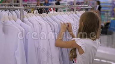 在服装店里挑选白色衬衫的少女。 时尚和购物